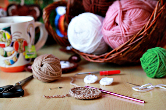 balls and skeins of yarn, crochet work, crochet hook, scissors, needle, and mug with tea on the table