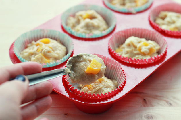 filling muffin liners with peach muffin batter in a muffin tin
